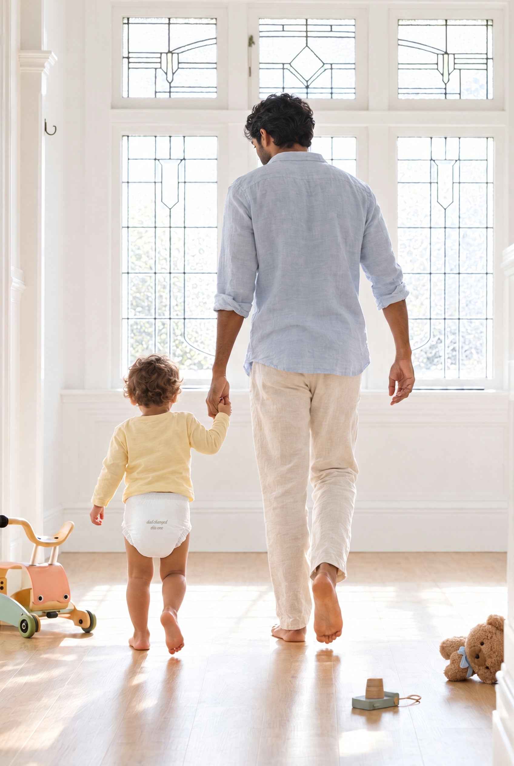 A dad walking hand in hand with his toddler toward a bright window, diaper printed dad changed this one